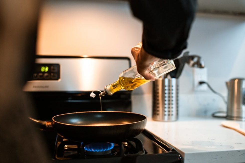 crop faceless chef pouring oil in pan